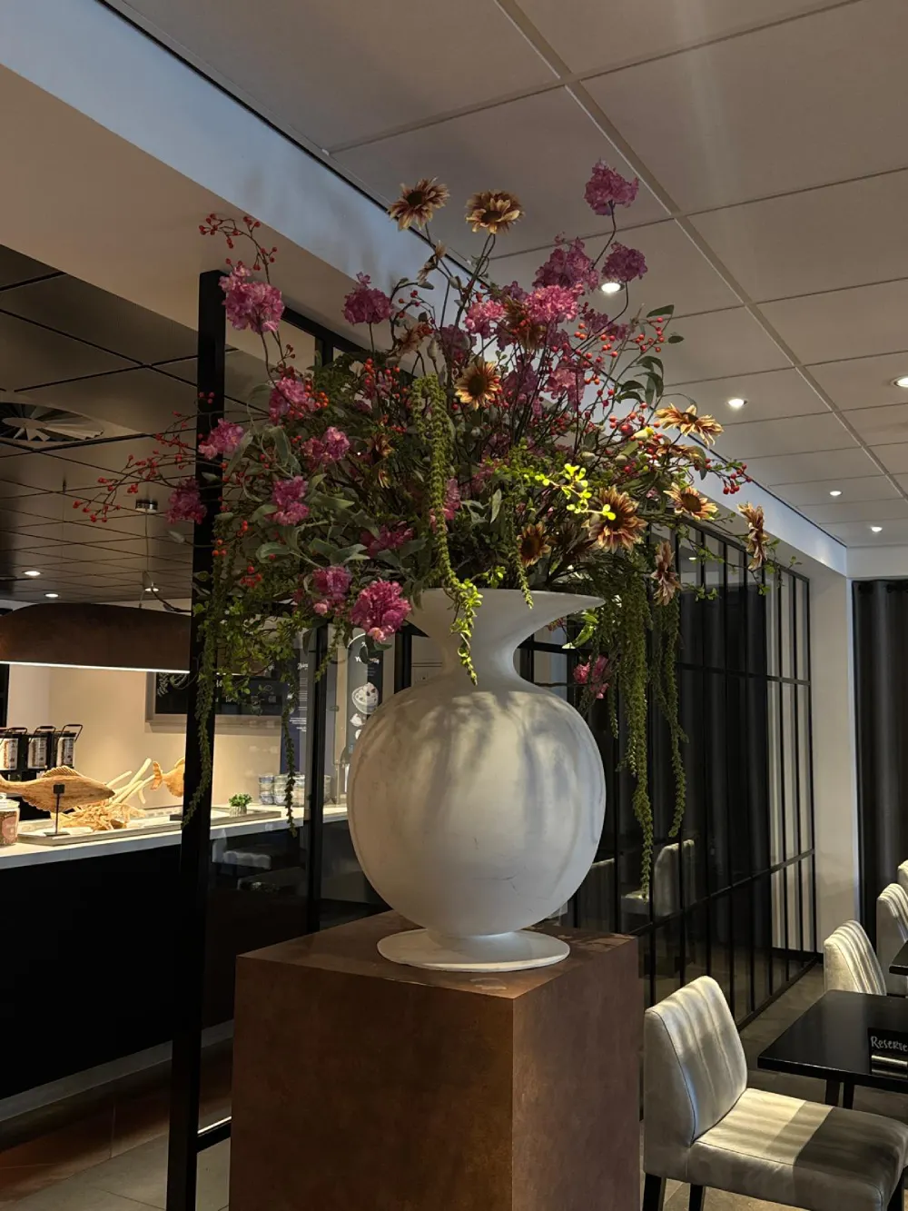 Bolvormig zijden bloemstuk op een bronzen zuil in een hotel- of restaurantlobby