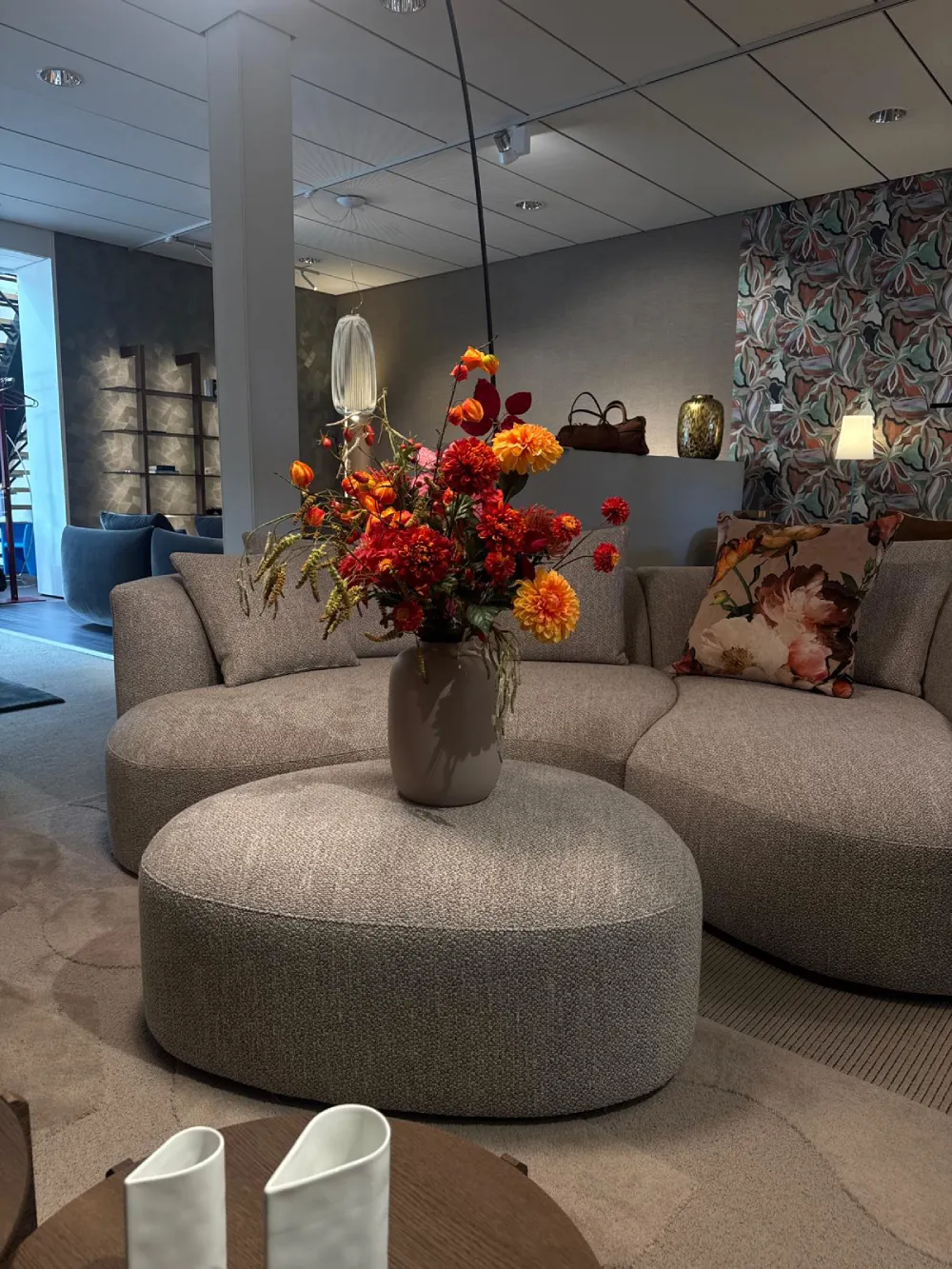 Warm zijden herfstarrangement in een showroom met poef en bank